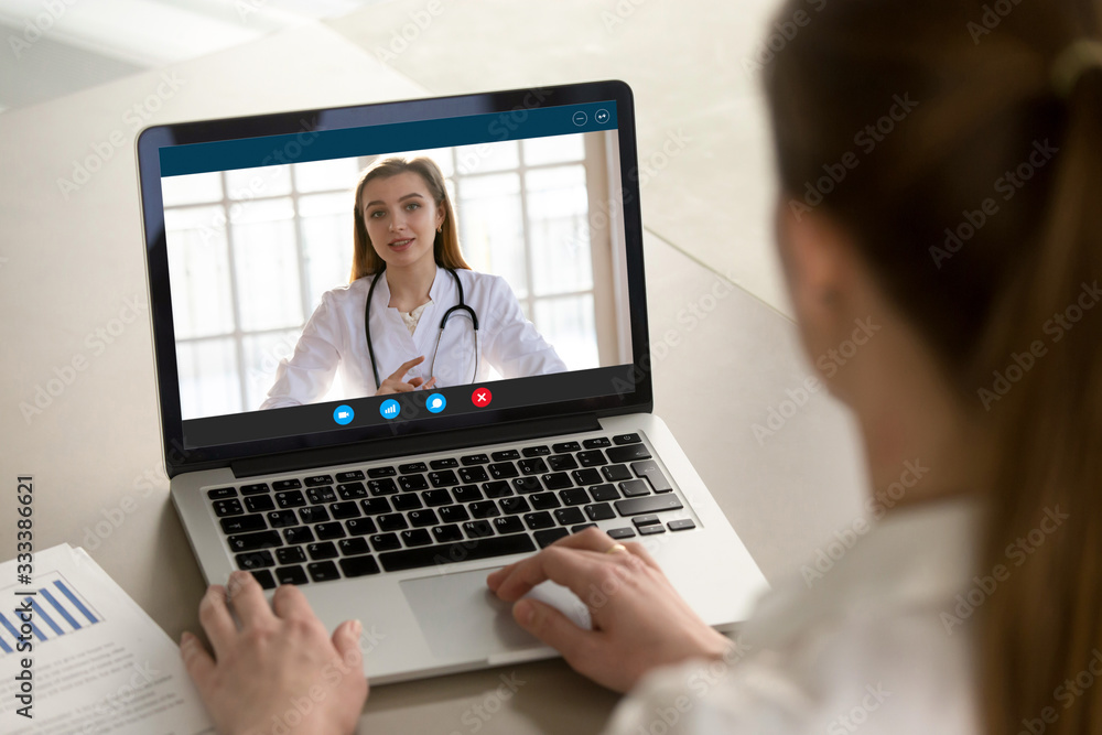 Shoulder view young woman consulting with family therapist doctor general practitioner online via video call on laptop after feeling first virus illness symptoms, medical insurance, covid19 outspread. - obrazy, fototapety, plakaty 