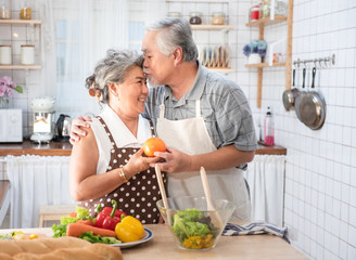 Senior couple having fun in kitchen with healthy food - Retired people cooking meal at home with man and woman preparing lunch with bio vegetables - Happy elderly concept with mature funny pensioner.