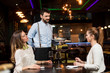© BGStock72 - Smiling young female friends at a restaurant with waiter serving dinner