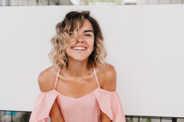 Portrait of stunning girl with wavy hair wears pink attire. Indoor photo of cheerful short-haired european woman laughing on light background.