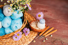 Women's Hobby. Crochet And Knitting. Working Space. Blue Yarn In Basket, Flowers, Knitting Needles, Scissors, Crochet Hooks On The Wooden Background In The Cozy Home In Rustik Style.