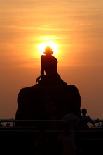 Silhouette Of A Statue Of Ghandi Sitting On A Rock In The Sunset