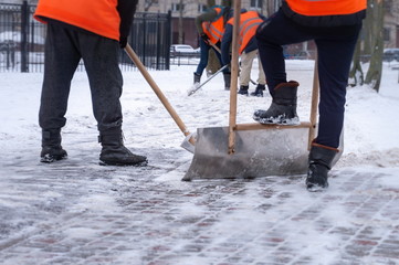 several janitors carefully cleans the yard from the snow with shovels while lazy workers stand and watch