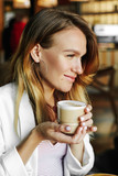 Fototapeta Tematy - Luxury girl in a cafe drinks coffee while walking in the city. Beautiful woman holding a mug of hot drink.