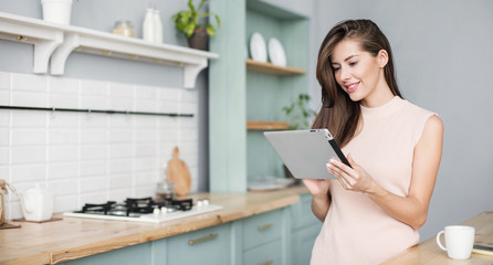 Beautiful young woman with digital tablet relaxing at home, Happy student girl using tablet pc in kitchen, Resting, relaxation, technology, online shopping, studying at home, learning online concept