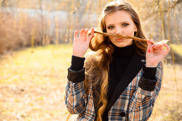 Portrait of a fashionable beautiful young girl with long hair with a smile in the park on a background of nature. Photo taken in sunny weather outdoors in spring.