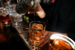 © fesenko - Close-up bartender masterfully pours old fashioned cocktail into glass on bar counter.