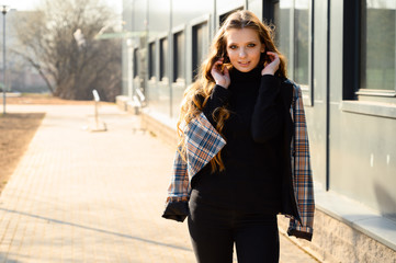 Portrait of a pretty beautiful young girl with long hair with a smile in the city against the background of the wall of a business building. Photo taken in sunny weather outdoors in spring.