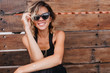 © Look! - Pleasant blonde woman posing in dark sunglasses on wooden background. Photo of attractive caucasian female model in black clothes smiling to camera.