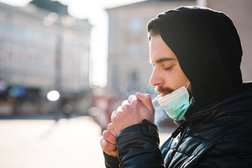 Coronavirus. Smoking. Closeup man with mask during COVID-19 pandemic smoking a cigarette at the street. Smoking causes lung cancer and other diseases. The dangers and harm of smoking.