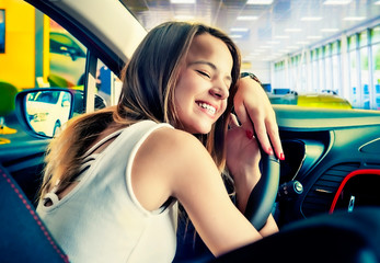 Young beautiful woman lying on an automobile rudder, closing eyes and hugging it. Happy client of car dealership after purchase of vehicle.