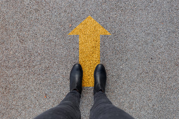 Black shoes standing on the asphalt concrete floor with yellow arrow. Feet shoes walking in outdoor. Youth Selphie Modern hipster