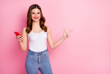 Wall Mural - Portrait of positive cheerful girl point index finger copyspace use cellphone recommend online sales discounts wear white singlet isolated over pink color background