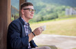 © Pituk - Handsome young man wearing glasses to drink coffee outdoors