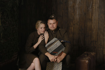 Portrait couple in military uniforms from the second world war young woman and man with accordion sit in embrace and near to them suitcase