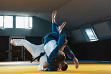 Two young judo caucasian fighters in white and blue kimono with black belts training martial arts in the gym with expression, in action, motion. Practicing fighting skills. Overcoming, reaching target