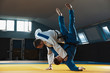 Two young judo caucasian fighters in white and blue kimono with black belts training martial arts in the gym with expression, in action, motion. Practicing fighting skills. Overcoming, reaching target