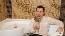 Man In A Shirt And Trousers In A Bath With Water Sings And Drinks Alcohol.