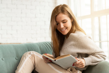 Cute woman sitting on cozy sofa and reads book