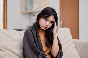 Wall Mural - Portrait of Young woman sitting on a couch, holding her head, having a strong headache. Pandemic 2019 Coronavirus 2019-nCoV Concept.