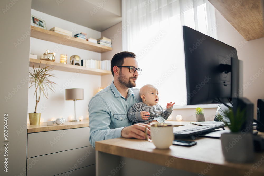 Young father working from home and babysitting his baby boy in the same time. - obrazy, fototapety, plakaty 