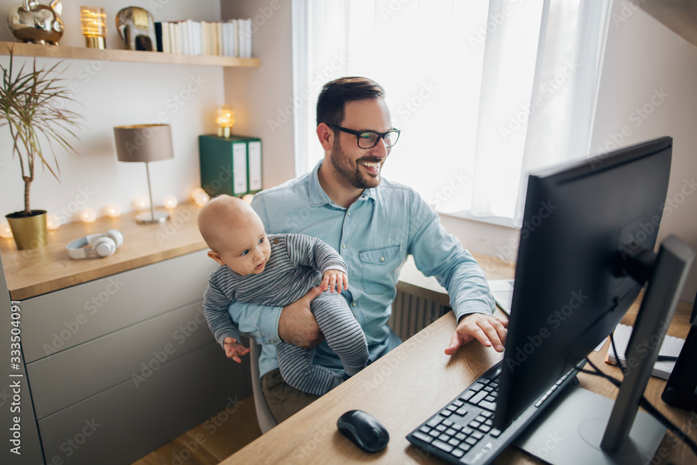 Young parent works from home and holds his baby boy. - obrazy, fototapety, plakaty 