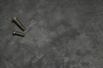 Two large bolts lie in a corner on a dark gray background with a beautiful texture. Industrial photophone for design and text.