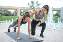 Fitness Young Woman Doing Push-ups With Assistance Of Her Female Personal Trainer Outdoors