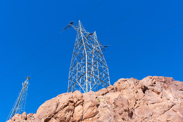 Wall Mural - High voltage transmission towers with parallel lines on the top of the rocky hill in the blue sky