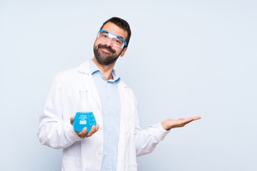 Wall Mural - Young scientific holding laboratory flask over isolated background presenting an idea while looking smiling towards
