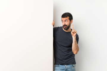Wall Mural - Young handsome man with beard holding a big empty placard intending to realizes the solution while lifting a finger up