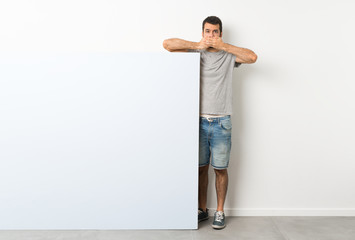 Wall Mural - Young handsome man with beard holding a big blue empty placard covering mouth with hands