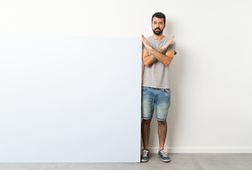 Wall Mural - Young handsome man with beard holding a big blue empty placard making NO gesture