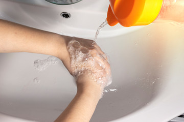 The girl washes her hands with soap under a stream of water from a jug. Close up