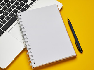 Workplace - laptop, notebook and pen for remote work on a yellow background table. Freelance desktop for home or office. Background with copy space.