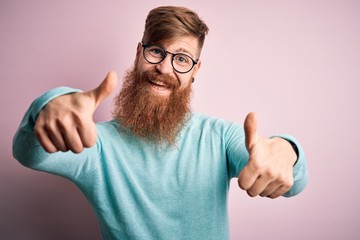 Poster - Handsome Irish redhead man with beard wearing glasses over pink isolated background approving doing positive gesture with hand, thumbs up smiling and happy for success. Winner gesture.