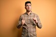 © Krakenimages.com - Young handsome man wearing casual shirt standing over isolated yellow background Pointing up looking sad and upset, indicating direction with fingers, unhappy and depressed.