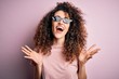 © Krakenimages.com - Young beautiful woman with curly hair and piercing wearing funny thug life sunglasses celebrating mad and crazy for success with arms raised and closed eyes screaming excited. Winner concept