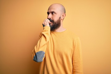 Poster - Handsome bald man with beard wearing casual sweater standing over yellow background looking stressed and nervous with hands on mouth biting nails. Anxiety problem.