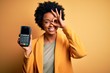 © Krakenimages.com - Young African American afro woman with curly hair holding dataphone payment device with happy face smiling doing ok sign with hand on eye looking through fingers