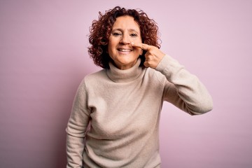 Sticker - Middle age beautiful curly hair woman wearing casual turtleneck sweater over pink background Pointing with hand finger to face and nose, smiling cheerful. Beauty concept