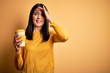 © Krakenimages.com - Young woman with blue eyes holding cup of coffee standing over yellow background stressed with hand on head, shocked with shame and surprise face, angry and frustrated. Fear and upset for mistake.