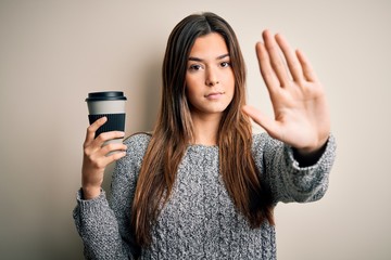 Poster - Young beautiful girl drinking cup of coffee standing over isolated white background with open hand doing stop sign with serious and confident expression, defense gesture