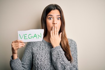 Sticker - Young beautiful girl holding paper with vegan message over isolated white background cover mouth with hand shocked with shame for mistake, expression of fear, scared in silence, secret concept