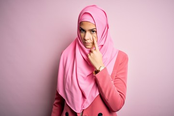 Poster - Young beautiful girl wearing muslim hijab standing over isolated pink background Pointing to the eye watching you gesture, suspicious expression