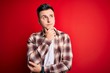 © Krakenimages.com - Young handsome caucasian man wearing casual modern shirt over red isolated background with hand on chin thinking about question, pensive expression. Smiling with thoughtful face. Doubt concept.