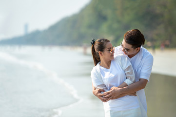 Wall Mural - Happy young Asian couple man hugging beautiful woman on tropical beach and looking at each other with smiling face. Healthy family people enjoying relax lifestyle in romantic summer holiday vacation.