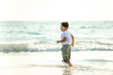 Wall Mural - Portrait Happy little Asian boy running and playing with smiling and laughing on tropical beach at sunset. Portrait of Adorable young child kids having fun in summer holiday vacation travel.