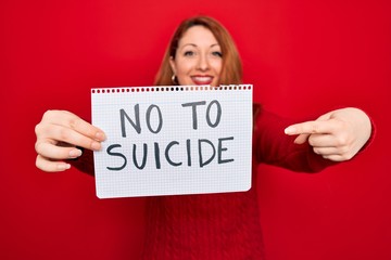 Sticker - Beautiful redhead woman holding banner showing no to suicide message over red background very happy pointing with hand and finger