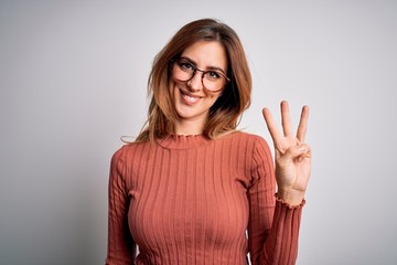 Young beautiful brunette woman wearing casual sweater and glasses over white background showing and pointing up with fingers number three while smiling confident and happy.